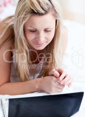 Serious woman using a laptop lying on a bed