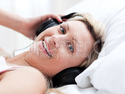 Positive woman with headphones on lying on a bed