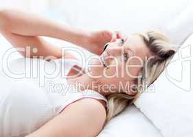 Smiling woman talking on phone lying on a bed