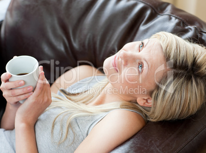 Charming woman drinking coffee sitting on a sofa