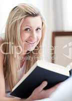 Jolly woman reading a book lying on her bed