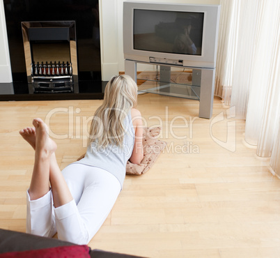 Blond woman watching TV lying on the floor