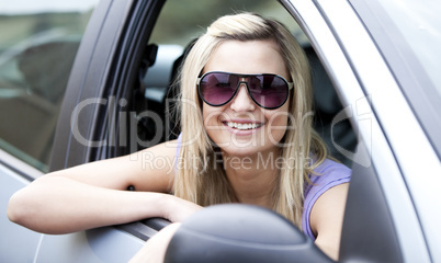 Jolly female driver wearing sunglasses sitting in her car