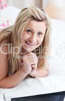 Smiling woman using a laptop lying on her bed