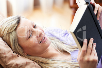 Jolly woman reading a book lying on a sofa