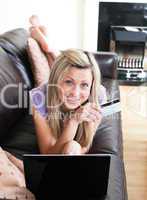 Smiling woman using a laptop lying on a sofa