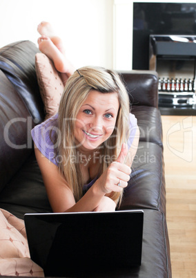 Happy woman using a laptop lying on a sofa