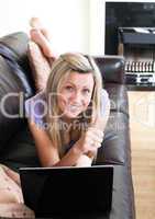 Happy woman using a laptop lying on a sofa