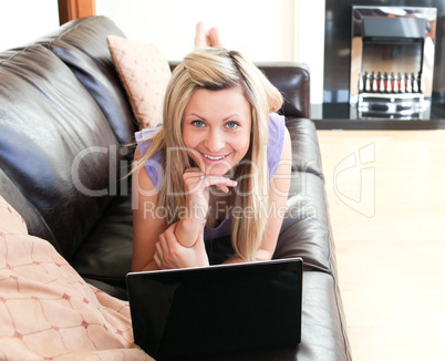 Smiling young woman using a laptop lying on a sofa