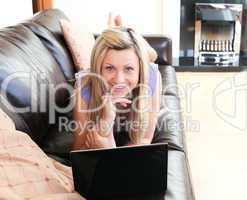Smiling young woman using a laptop lying on a sofa