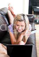 Cheerful woman using a laptop lying on a sofa