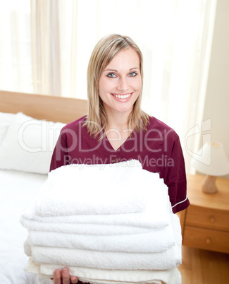 Smiing cleaning lady holding towels in a hotel room