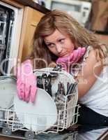 Tired young woman filing the dishwasher