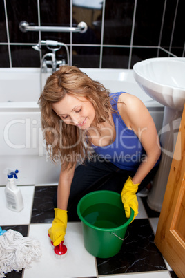 Smiling young woman cleaning bathroom's floor