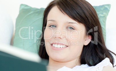 Cheerful woman reading a book lying on a sofa