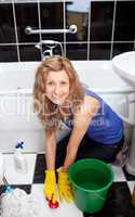 Positive young woman cleaning bathroom's floor