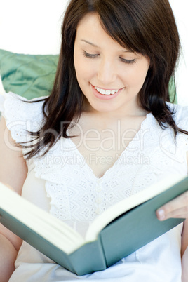 Radiant woman reading a book lying on a sofa