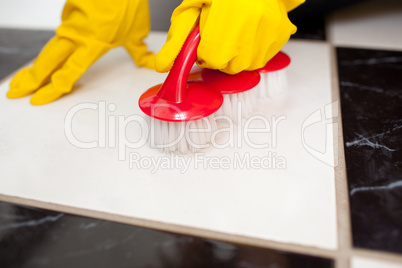 A person cleaning a bathroom's floor with a yellow rubber glove