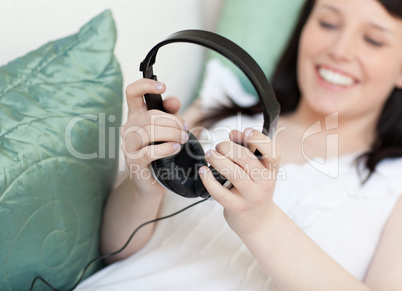 Cheerful young woman putting headphones lying on a sofa