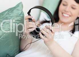 Cheerful young woman putting headphones lying on a sofa