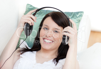 Jolly woman putting headphones lying on a sofa