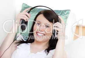 Jolly woman putting headphones lying on a sofa