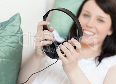 Smiling young woman putting headphones lying on a sofa