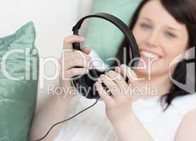 Smiling young woman putting headphones lying on a sofa