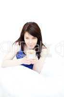 Smiling attractive woman drinking a coffee sitting on her bed