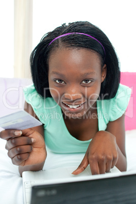 Cheerful woman shopping on-line lying on her bed