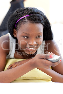 Cheerful young woman watching TV lying on a sofa