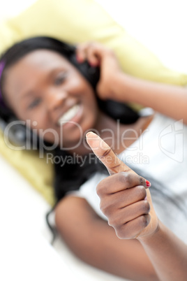 Smiling woman listening music with thumb up lying on a sofa