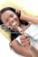 Smiling woman listening music with thumb up lying on a sofa