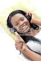 Happy woman listening music with thumb up lying on a sofa