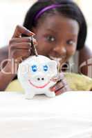 Cheerful teen girl putting money in a piggy-bank