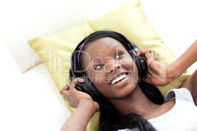 Smiling woman listening music with headphones lying on a sofa