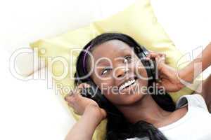 Smiling woman listening music with headphones lying on a sofa