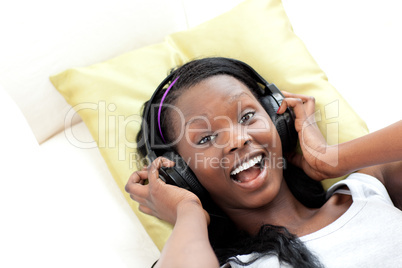 Laughing woman listening music with headphones lying on a sofa