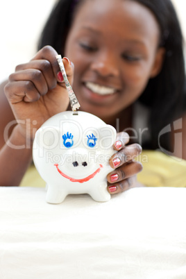 Afro-american teen girl putting money in a piggy-bank