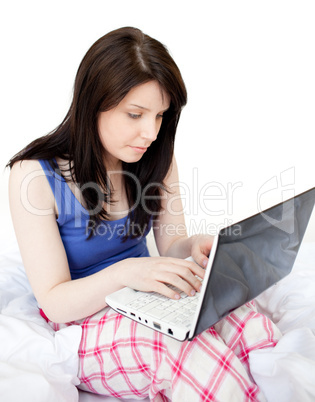 Concentrated woman using a laptop sitting on bed