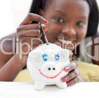 Smiling teen girl putting money in a piggy-bank