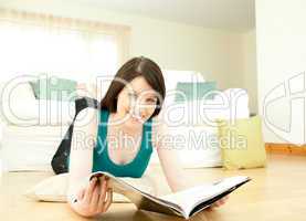 Brunette woman reading a magazine lying down on the floor