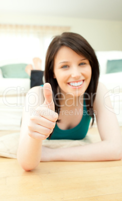 Positive woman with thumbs up lying on the floor