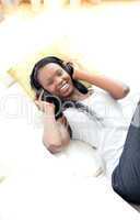 Radiant woman listening music with headphones lying on a sofa