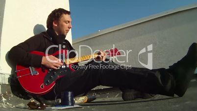 Man is sitting on the roof playing the guitar