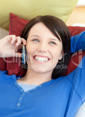 Happy young woman talking on phone lying on a sofa