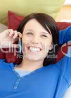 Happy young woman talking on phone lying on a sofa