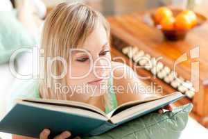 Serious woman reading a book lying on a sofa
