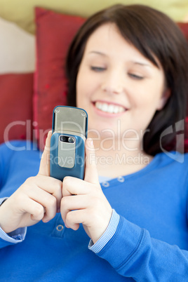 Cheerful teen girl sending a text lying on a sofa