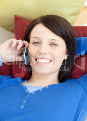 Jolly teen girl talking on phone lying on a sofa